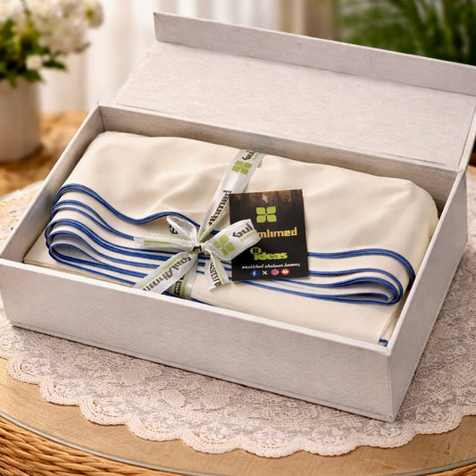 White towel with blue stripes in a white box on a wooden table with a plant and flowers in the background.